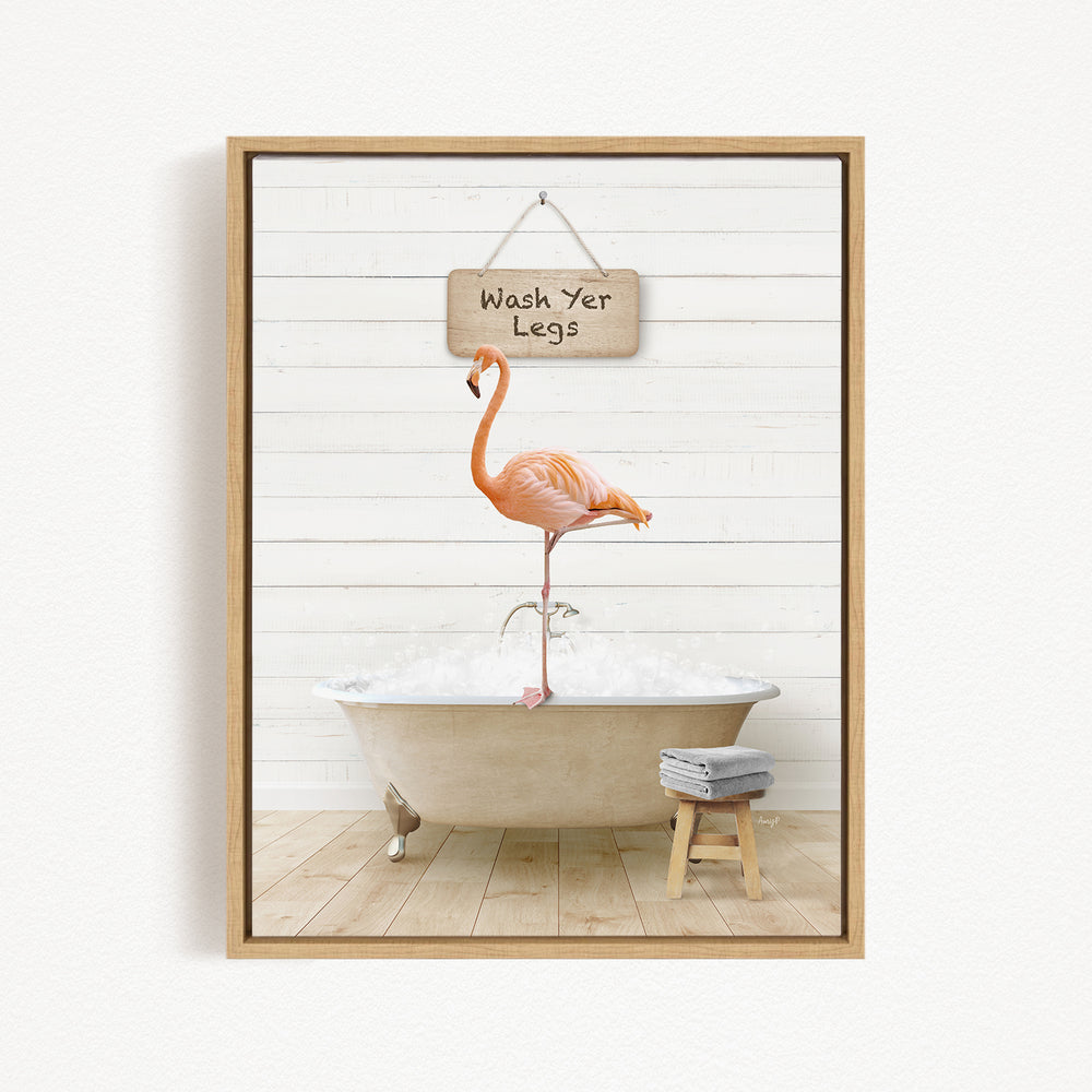A framed image depicting a pink flamingo standing on one leg inside a bathtub, with a sign above that says "Wash Your Legs".