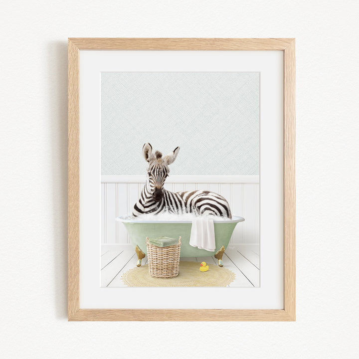 A zebra is sitting in a green bathtub filled with water, surrounded by a basket of toys and a yellow rubber ducky.