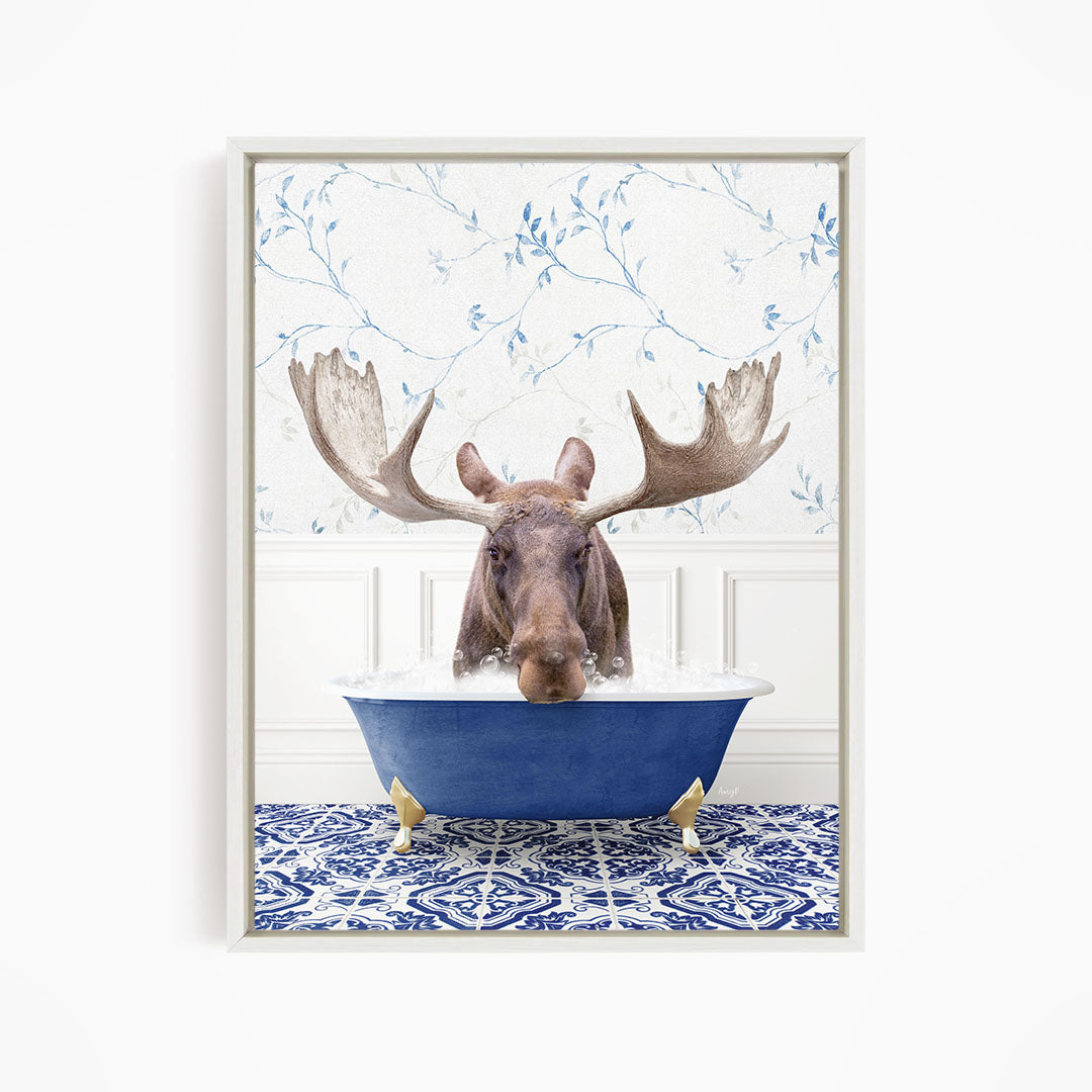 A moose with large antlers is sitting in a blue bathtub, surrounded by a patterned tile floor and a floral wallpaper background.