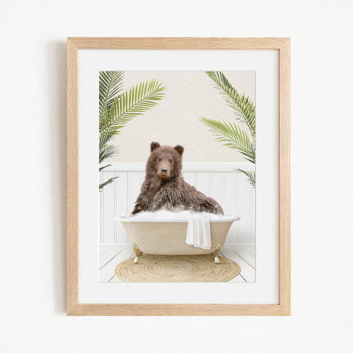 A brown bear sitting in a bathtub filled with bubbles, surrounded by green palm leaves.