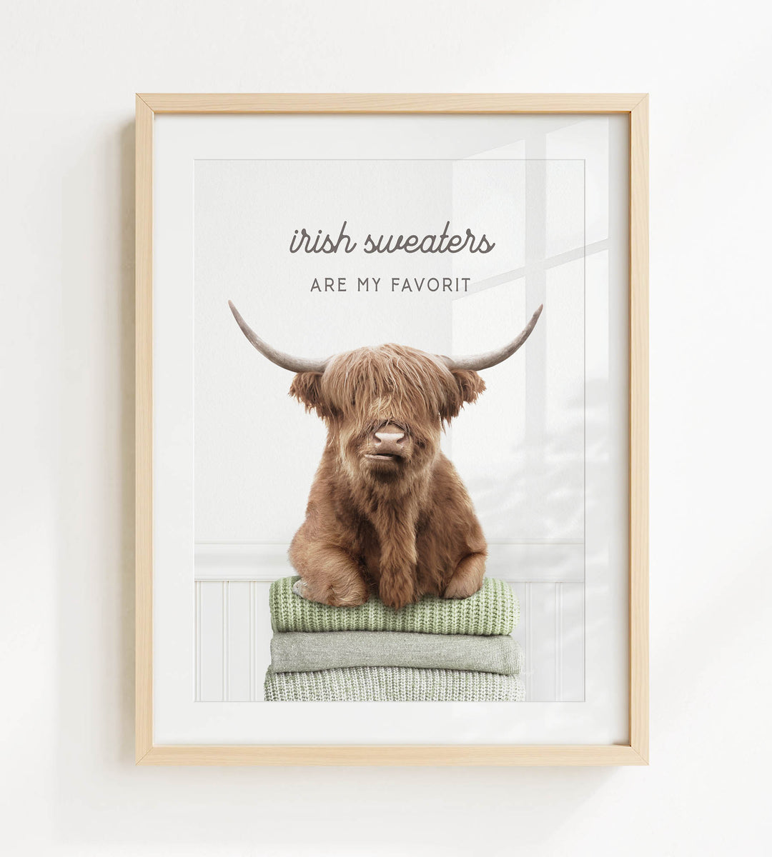 a brown cow with long horns sitting on a stack of green and white sweaters, with the text "Irish sweaters are my favorite" above the cow.