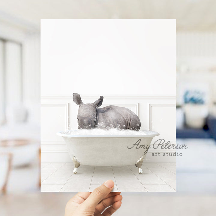 a hand holding up a photo of a rhino in a bathtub