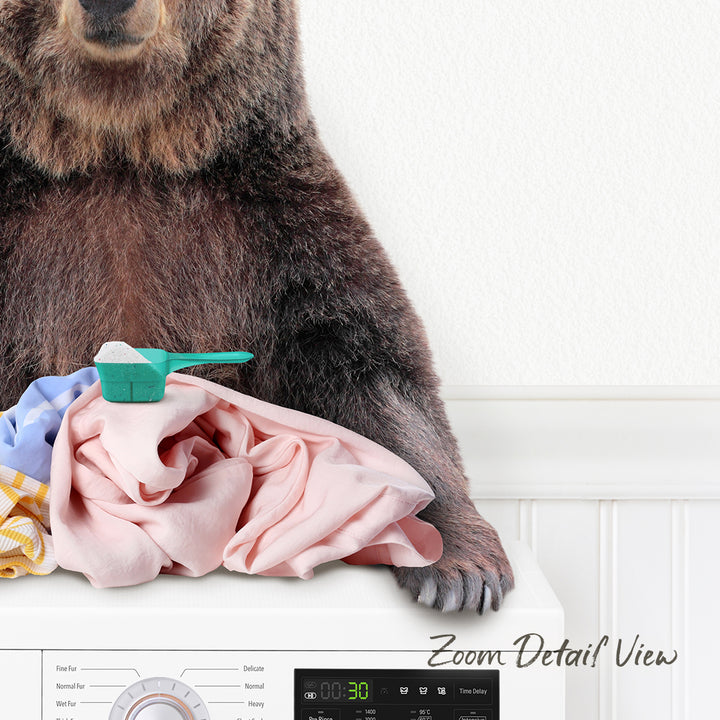 A brown bear is sitting on top of a pile of laundry next to a washing machine.