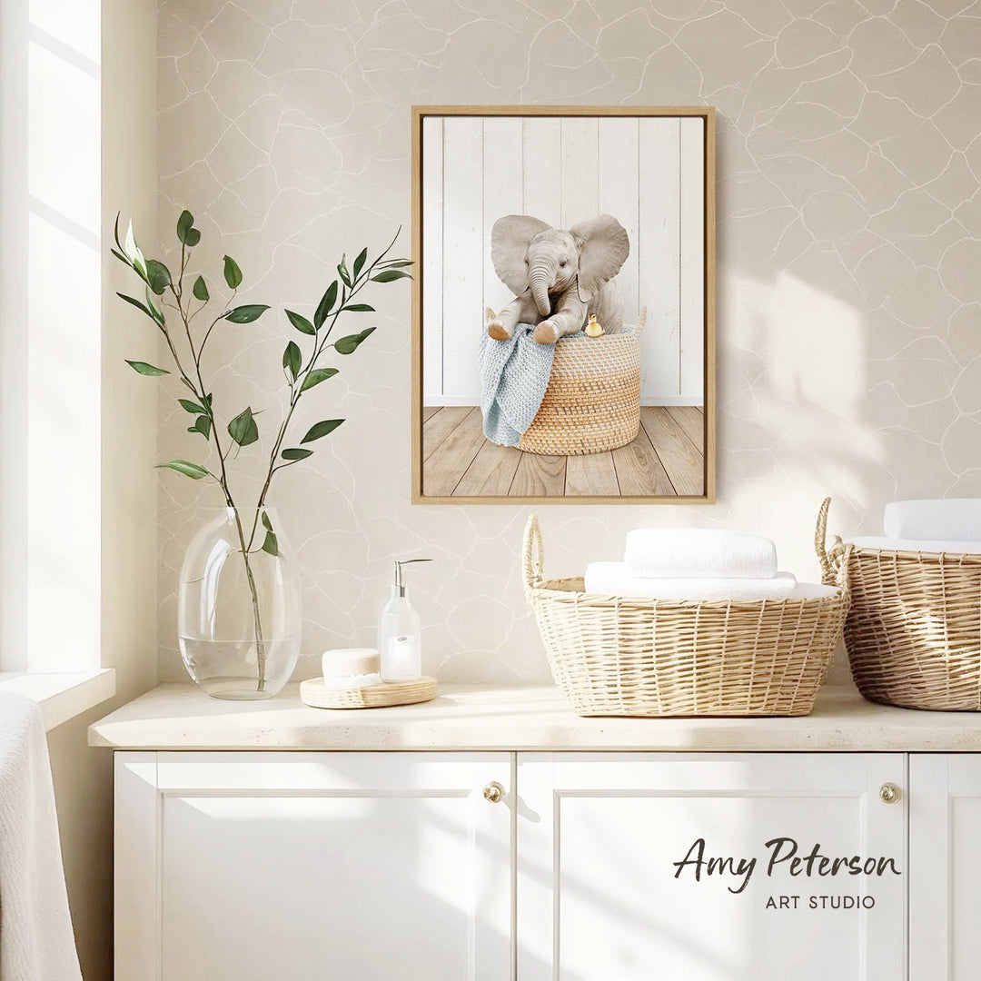 a framed picture of an elephant sitting in a basket, placed on a wall above a white cabinet with two woven baskets on top.