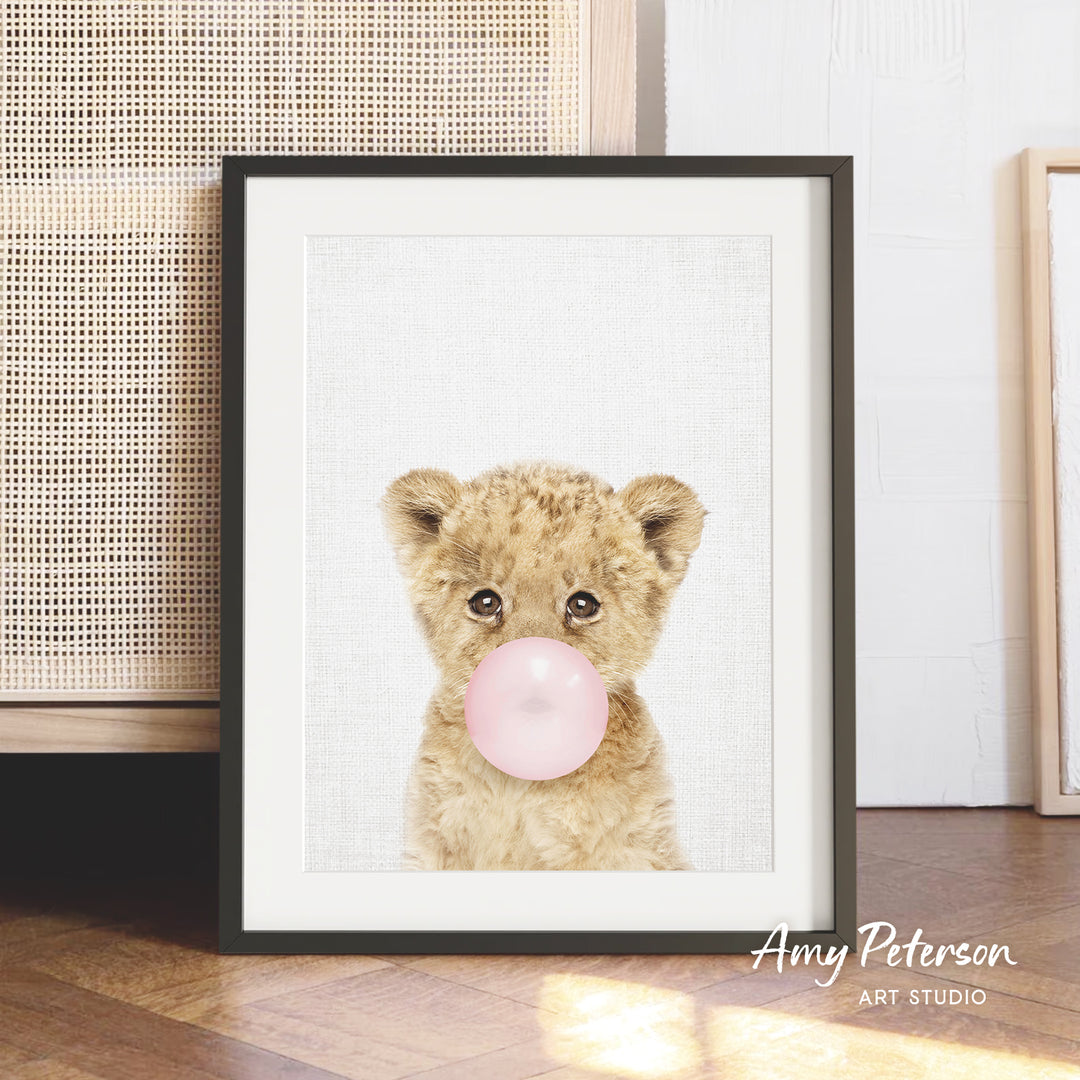 A framed print of a cute, fluffy animal blowing a bubble with a pink bubble gum bubble.
