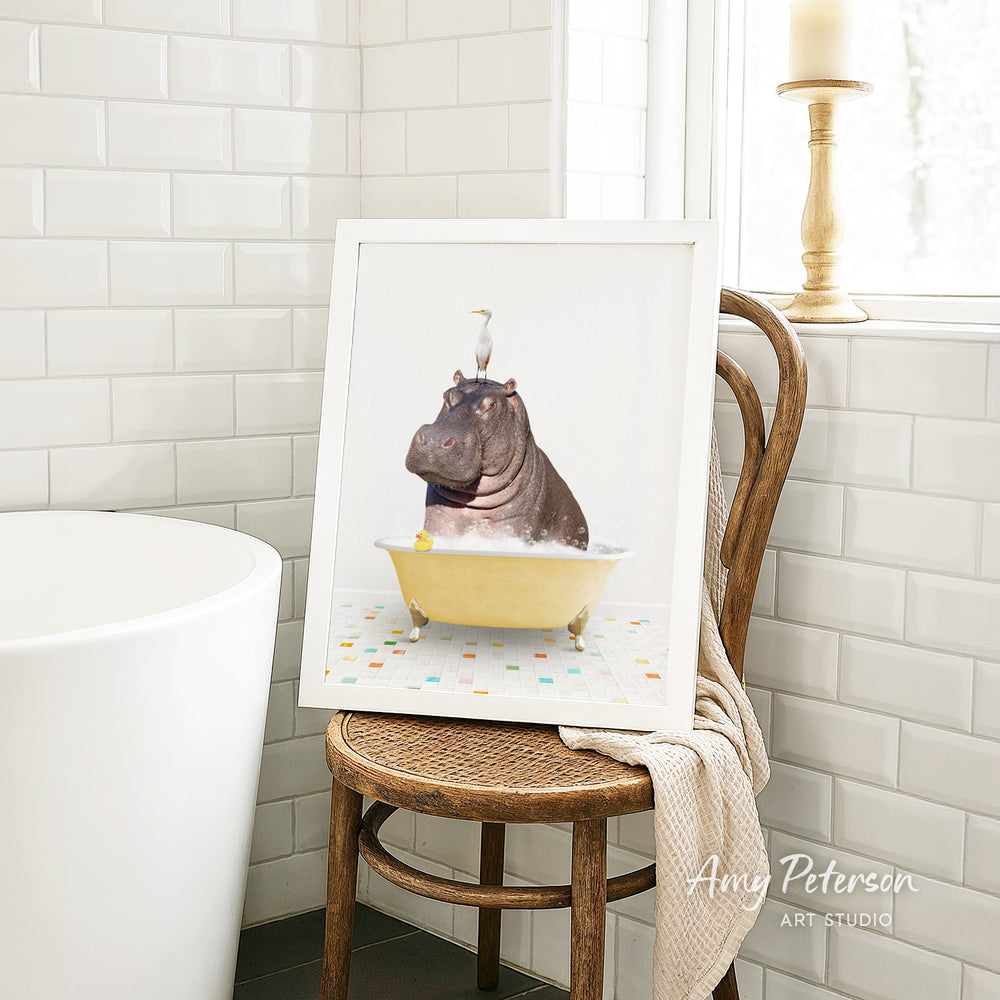 A framed image of a hippopotamus sitting in a bathtub, with a bird perched on its head, is displayed on a wooden chair in a bathroom setting.