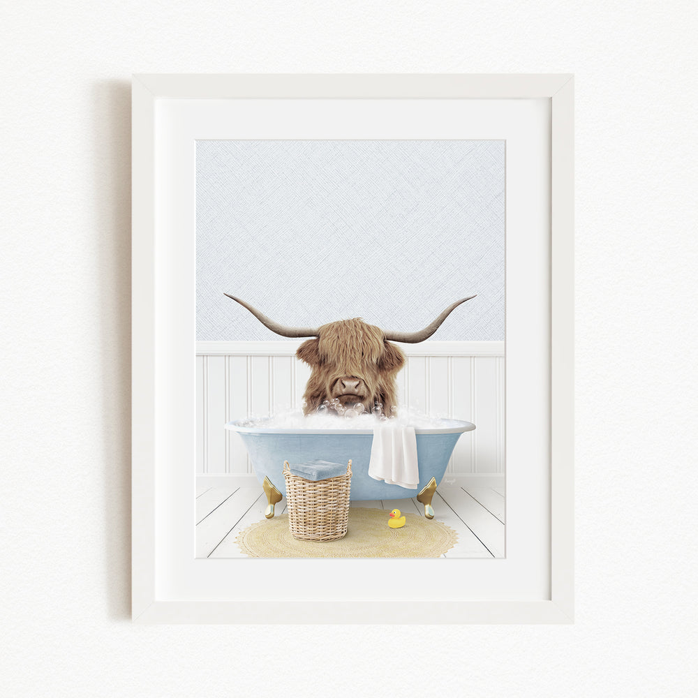 A framed image depicting a Highland cow with large horns sitting in a bathtub filled with water and surrounded by various objects, including a yellow rubber duck.