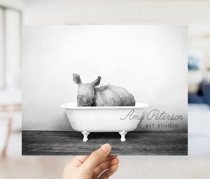 a hand holding up a black and white photo of a rhino in a bathtub