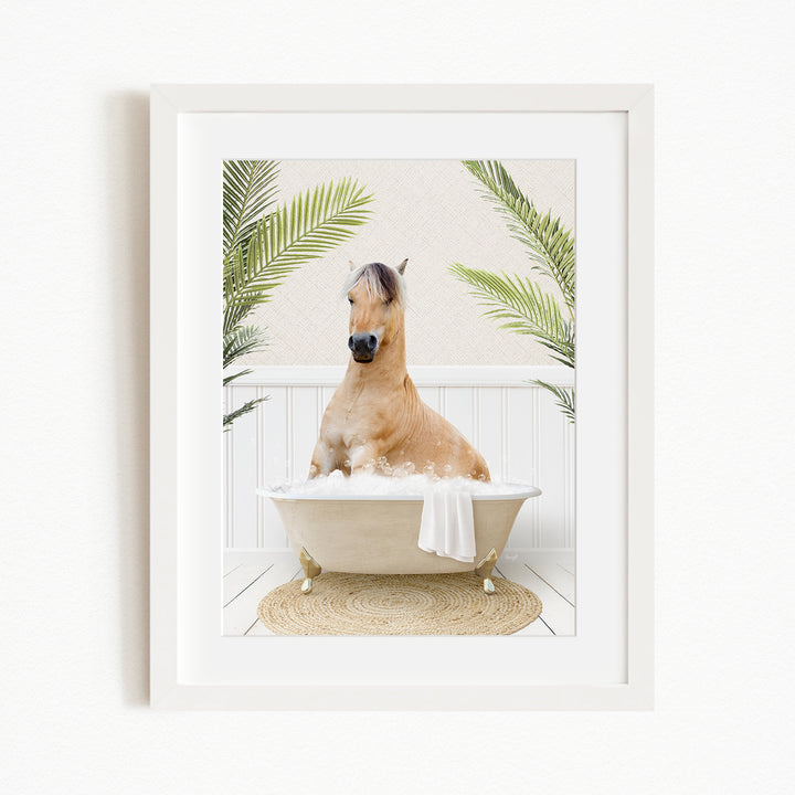 A light brown horse is sitting in a white bathtub filled with water, surrounded by green palm leaves.