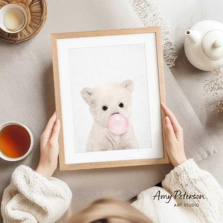 A person is holding a framed picture of a white bear blowing a bubble with a pink bubblegum bubble.