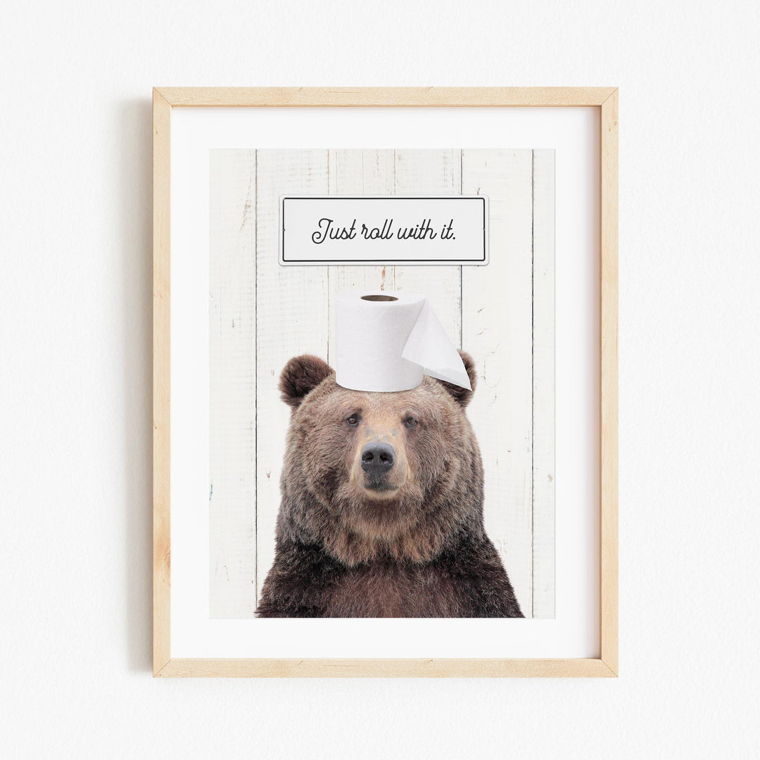A framed image of a brown bear wearing a toilet paper hat, with the text "Just roll with it."