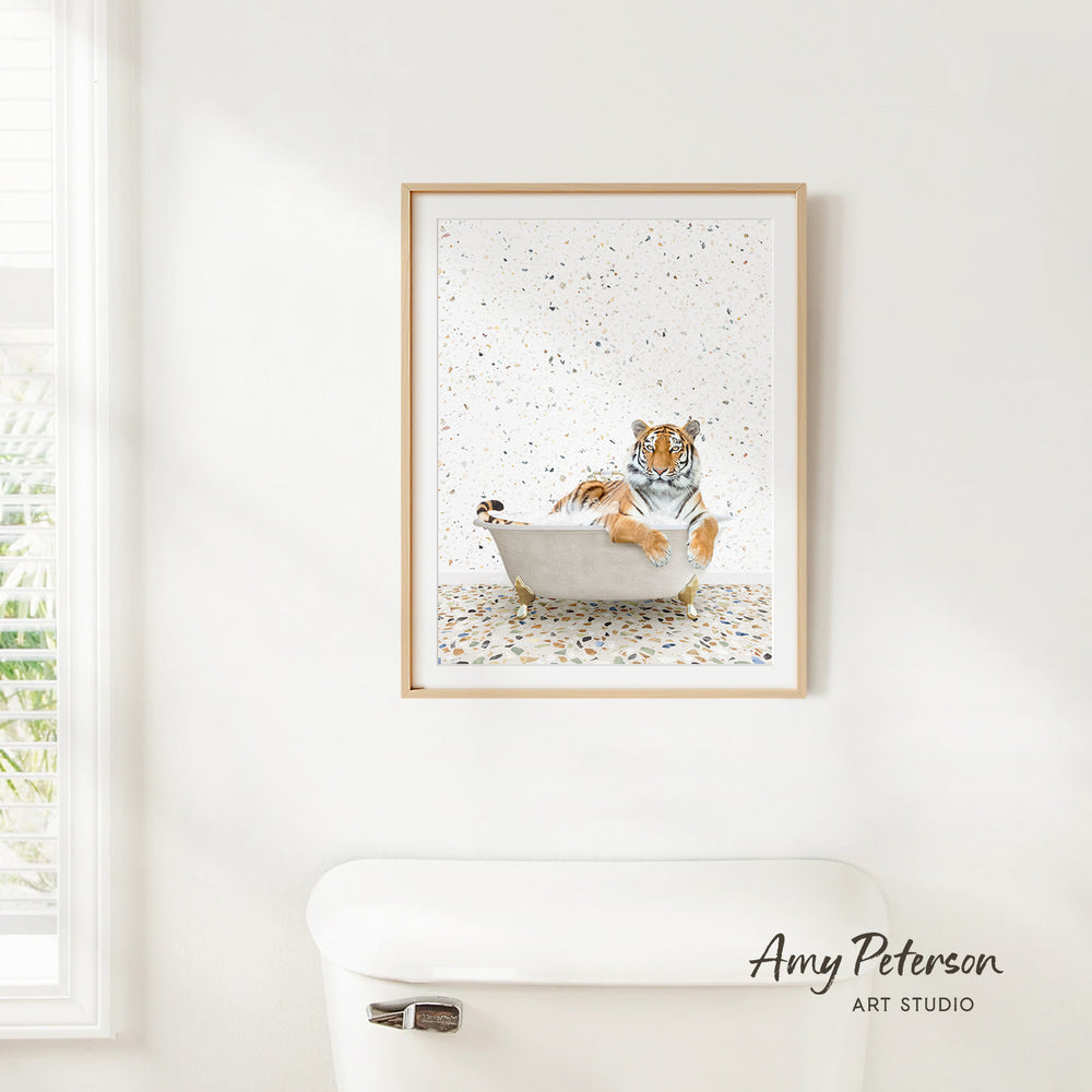 A framed print of a tiger sitting in a bathtub, surrounded by confetti, hangs on a white wall.