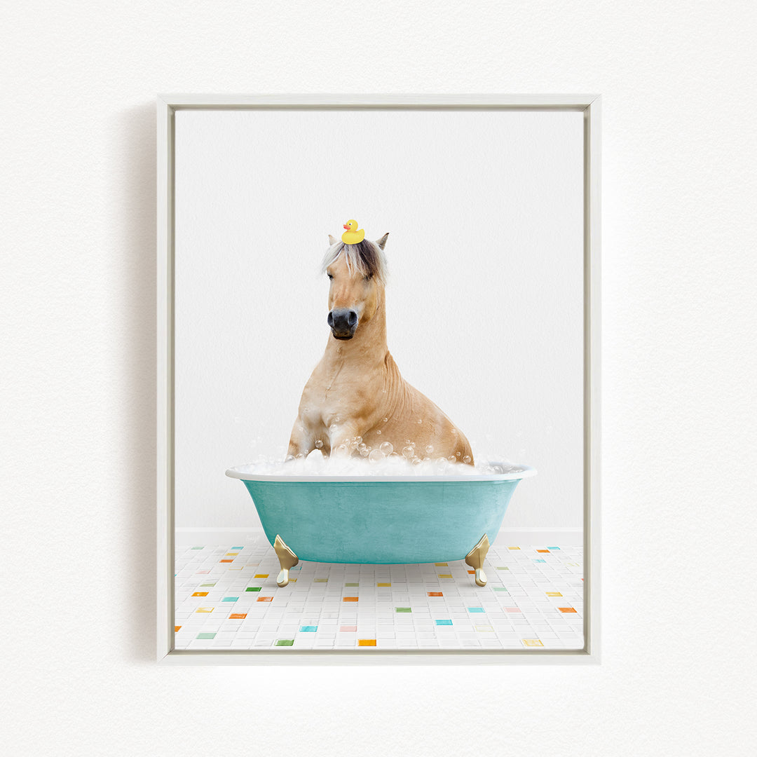 A light brown horse is sitting in a blue bathtub filled with bubbles, wearing a yellow rubber duck on its head.