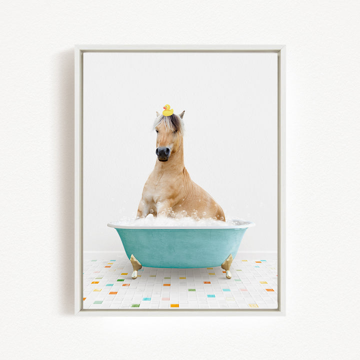 A light brown horse is sitting in a blue bathtub filled with bubbles, wearing a yellow rubber duck on its head.
