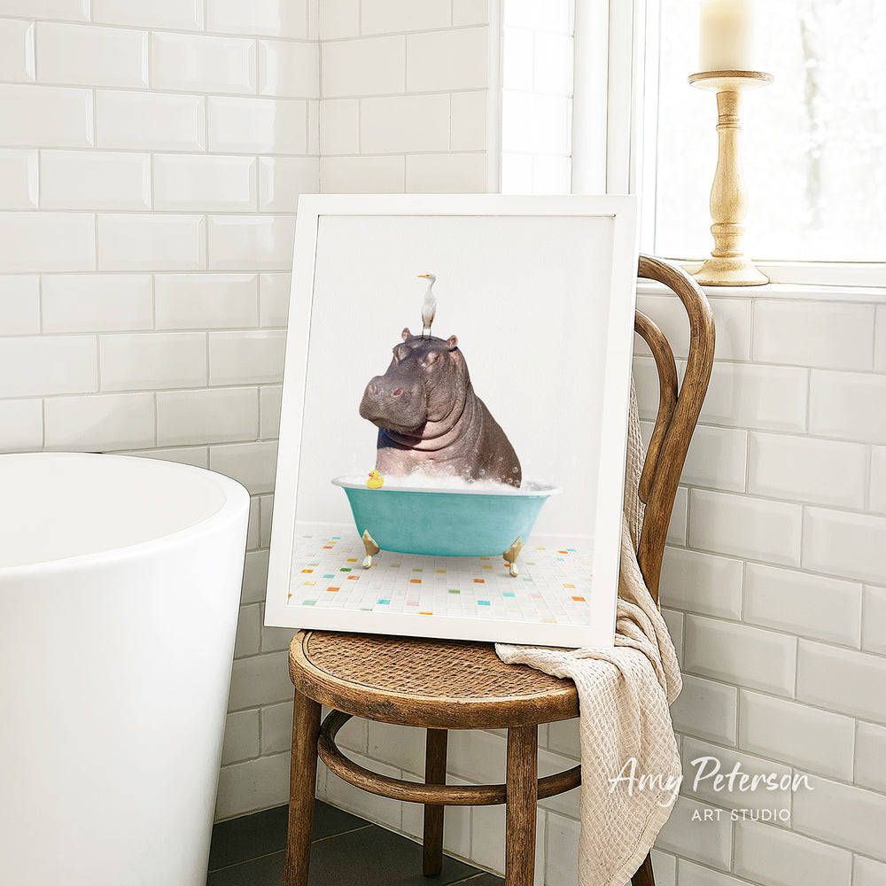 A framed image of a hippopotamus sitting in a bathtub, surrounded by colorful tiles, is displayed on a wooden chair in a bathroom setting.