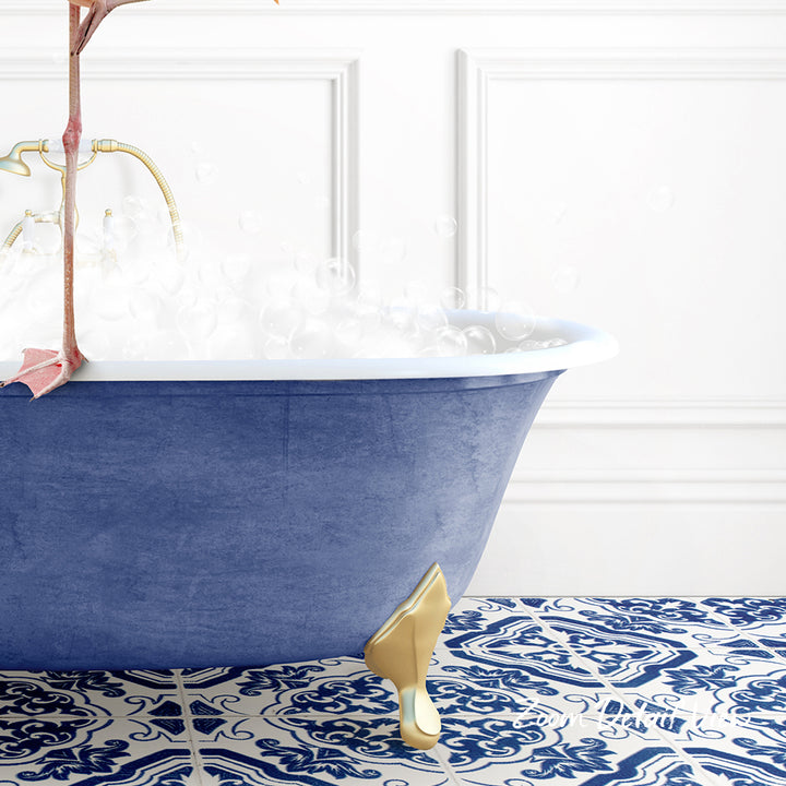 A blue clawfoot bathtub filled with water and bubbles, with a gold clawfoot design on the side, set against a white wall with a patterned tile floor.