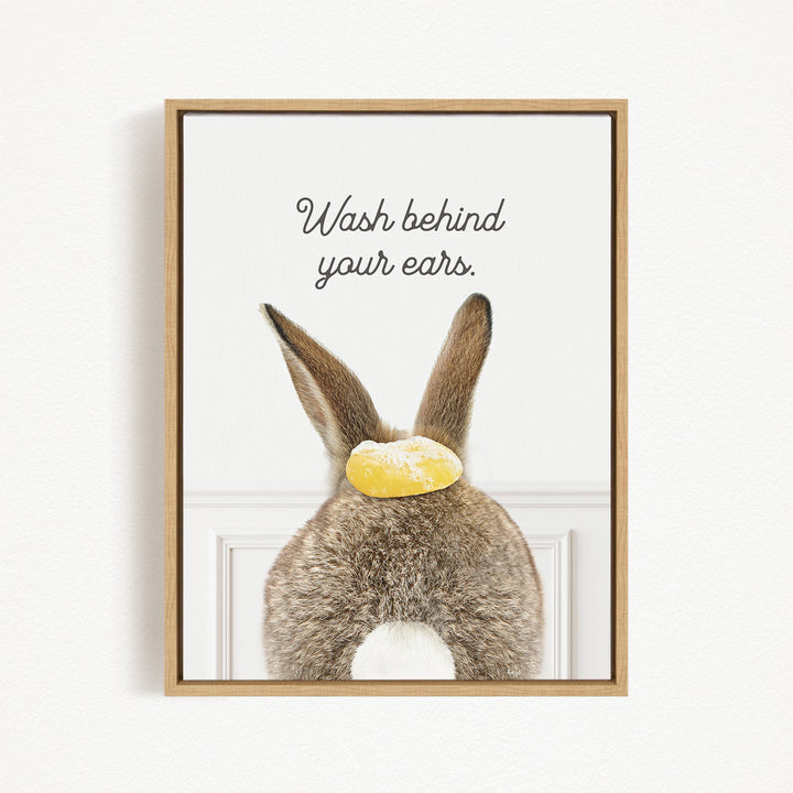 A framed image of a rabbit with a yellow object on its head, accompanied by the text "Wash behind your ears."