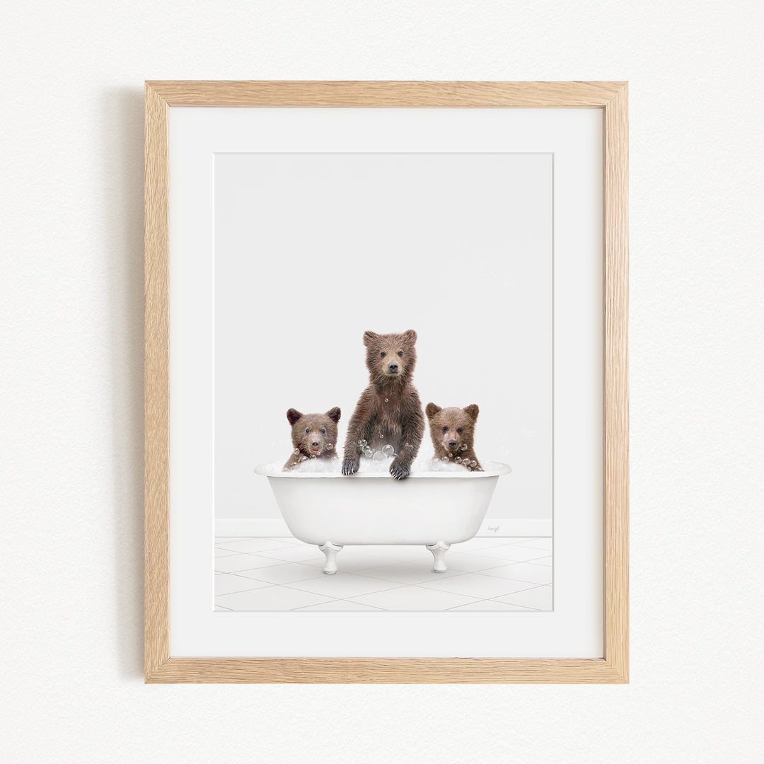 A framed image depicting three brown bears sitting in a white bathtub.