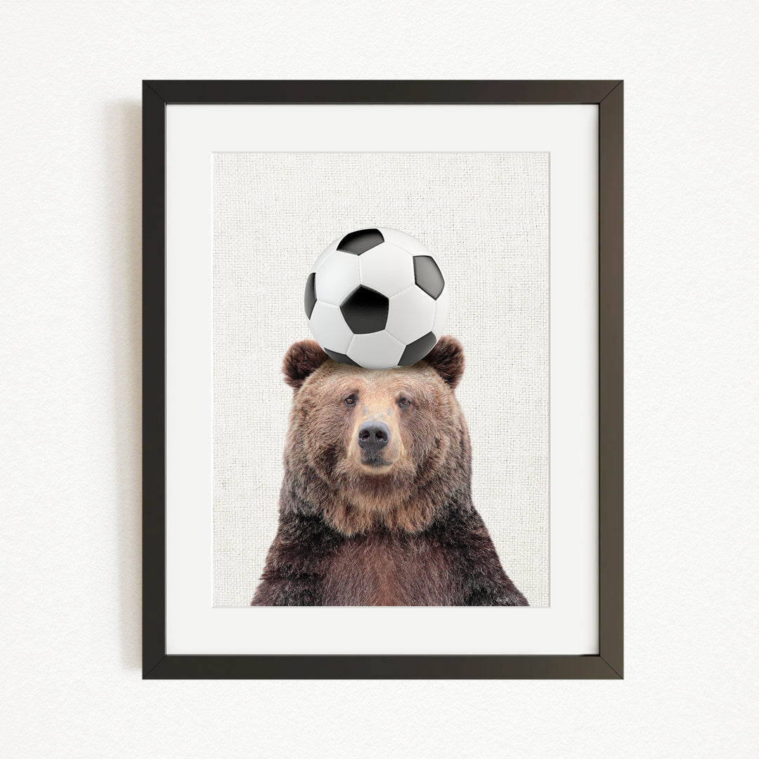 A brown bear balancing a soccer ball on its head.