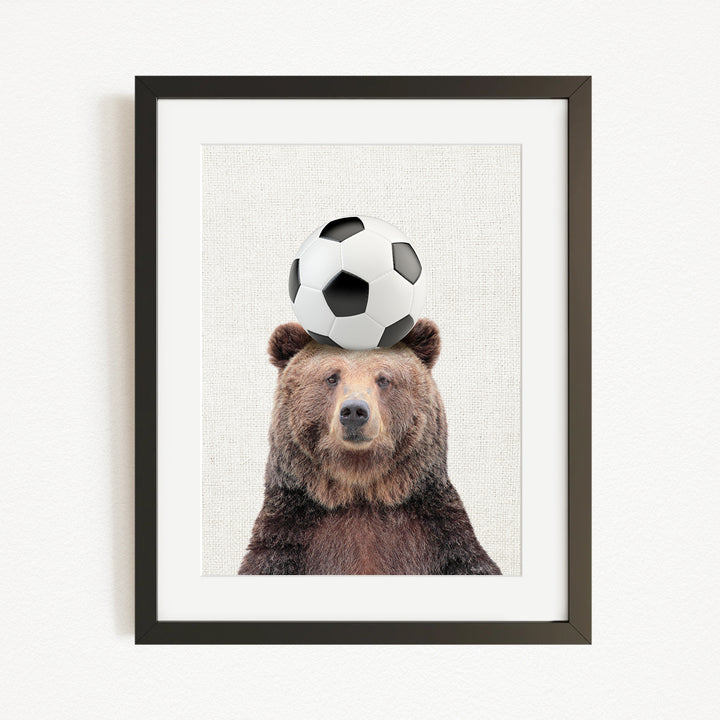A brown bear balancing a soccer ball on its head.