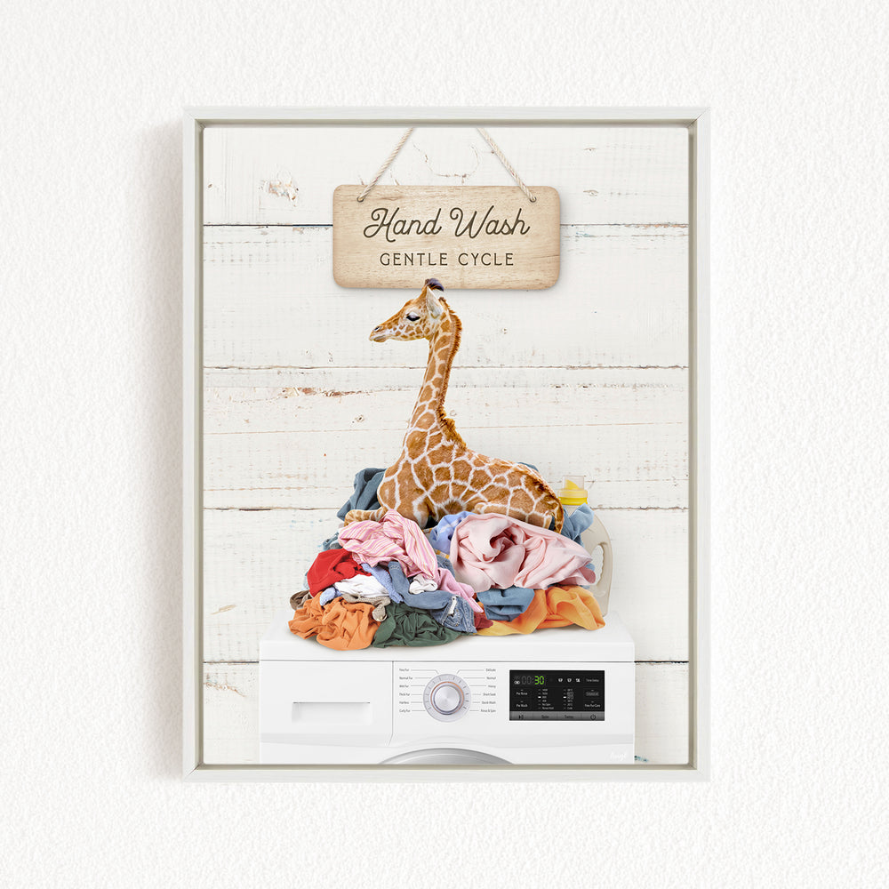 A giraffe sitting atop a pile of laundry, with a sign above that reads "Hand Wash Gentle Cycle".