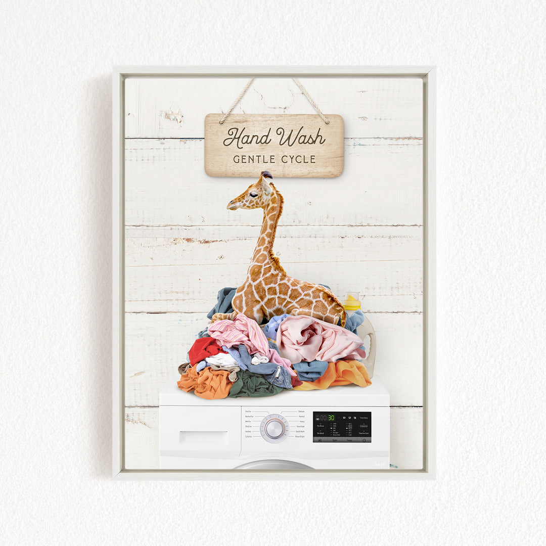 A giraffe sitting atop a pile of laundry, with a sign above that reads "Hand Wash Gentle Cycle".