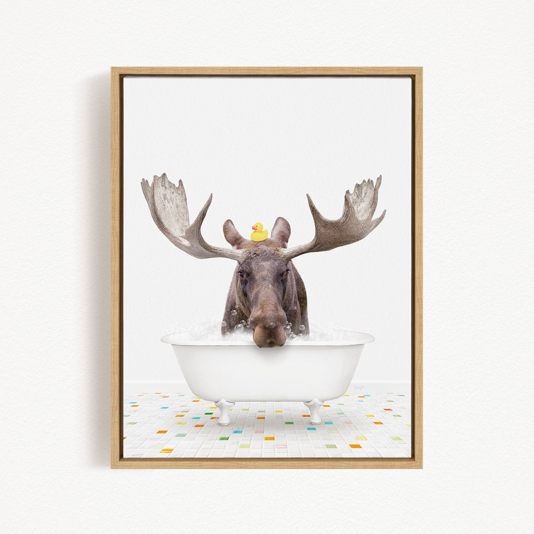 A moose with large antlers is sitting in a white bathtub, with a yellow rubber duck perched on its head.