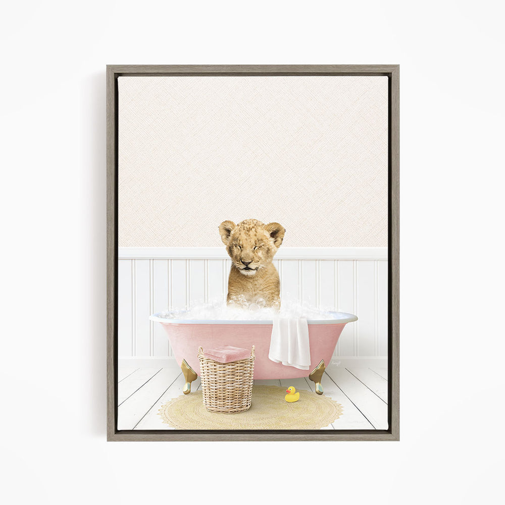 A young lion cub sitting in a pink bathtub filled with bubbles, surrounded by a yellow rubber duck and a basket.