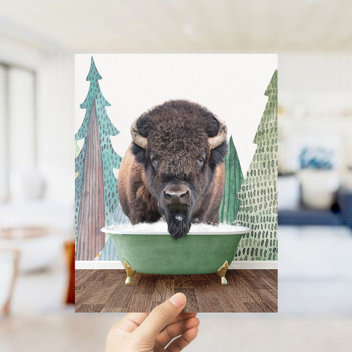 A bison with large horns is sitting in a green bathtub, surrounded by trees and a snowy landscape.