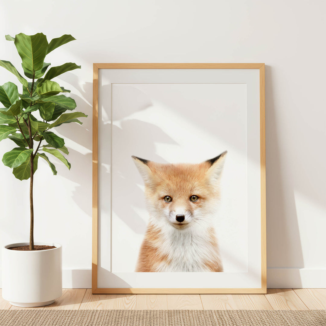 a framed photograph of a fox, with a potted plant to the left and a wooden floor to the right.