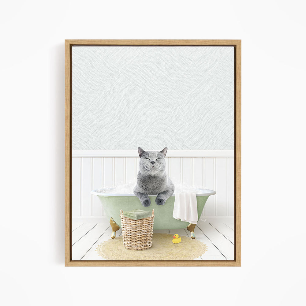 A gray cat sitting in a green bathtub filled with bubbles, with a basket of bath toys and a yellow rubber duck nearby.