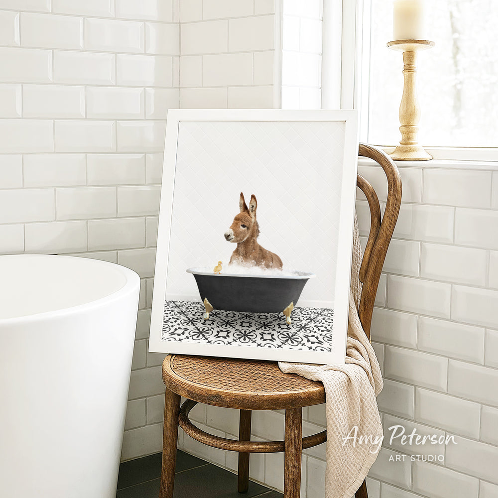 A framed image of a dog sitting in a bathtub, surrounded by a patterned tile floor, is displayed on a wooden chair in a bathroom setting.