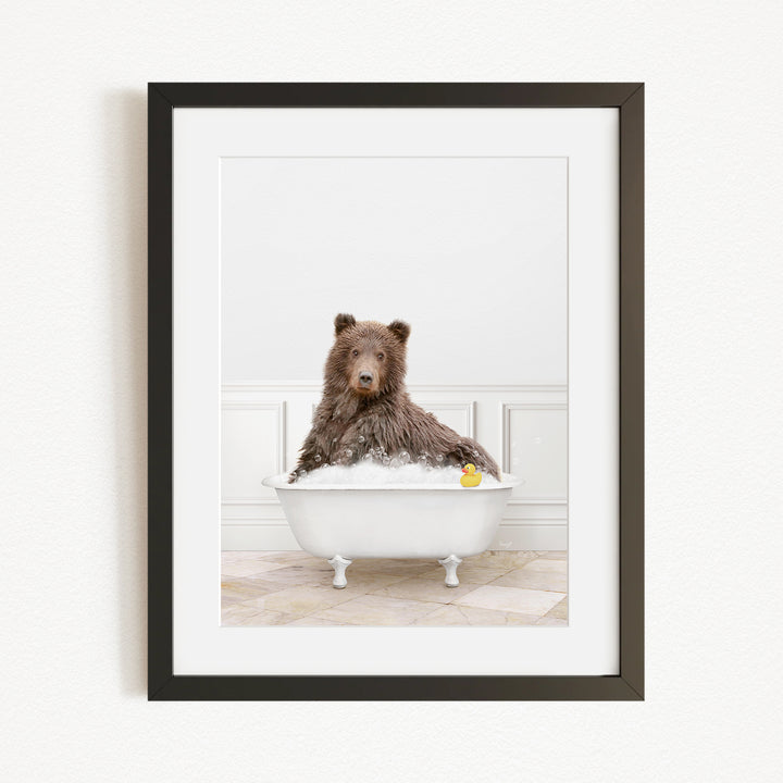 A brown bear sitting in a white bathtub, with a yellow rubber duck floating in the water.