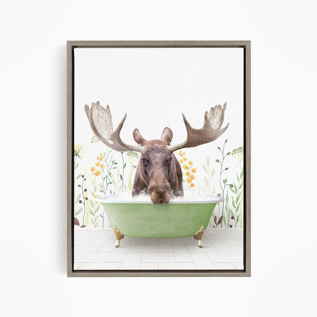 A moose with large antlers is sitting in a green bathtub, surrounded by flowers and plants.