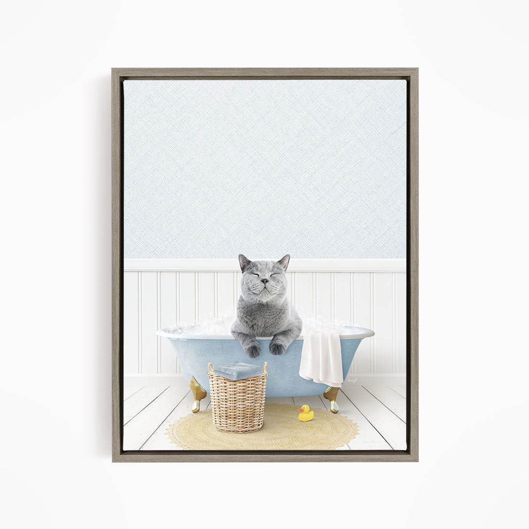 A gray cat sitting in a blue bathtub filled with bubbles, surrounded by a yellow rubber duck and a basket.