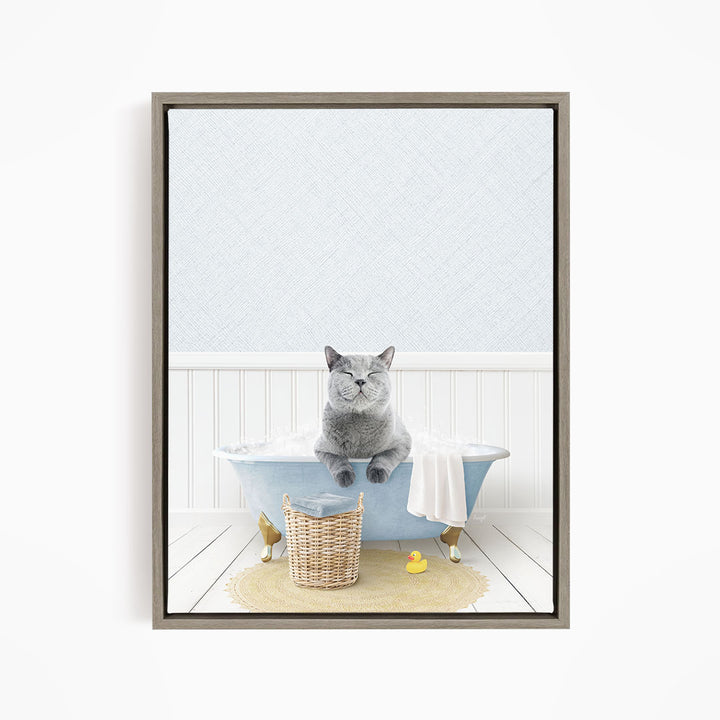 A gray cat sitting in a blue bathtub filled with bubbles, surrounded by a yellow rubber duck and a basket.