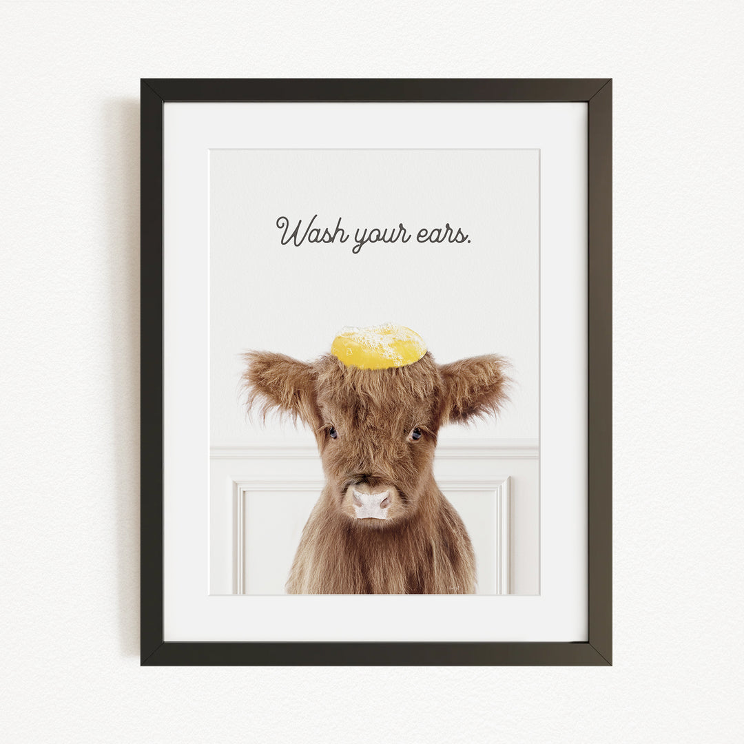 A framed image of a brown cow with a yellow object on its head, accompanied by the text "Wash your ears."