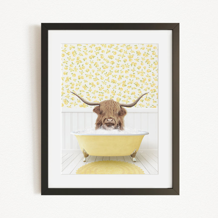 A framed print depicting a Highland cow with long horns sitting in a yellow bathtub, surrounded by a yellow floral pattern on the wall behind it.