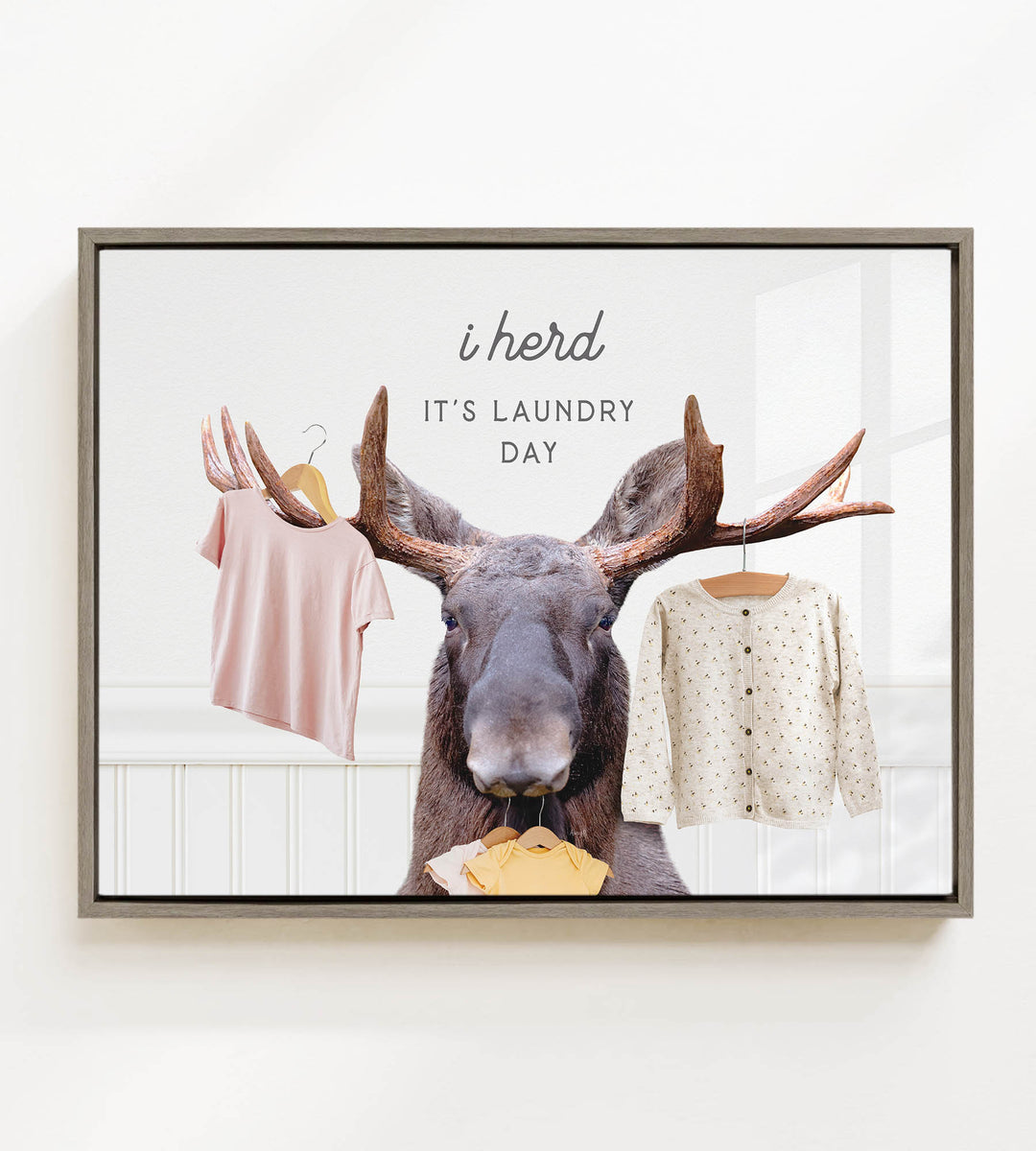 A framed image depicting a moose holding clothes, with the text "i herd, it's laundry day" above it.