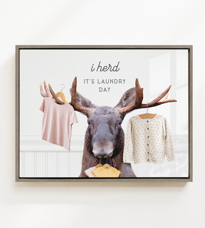 A framed image depicting a moose holding clothes, with the text "i herd, it's laundry day" above it.