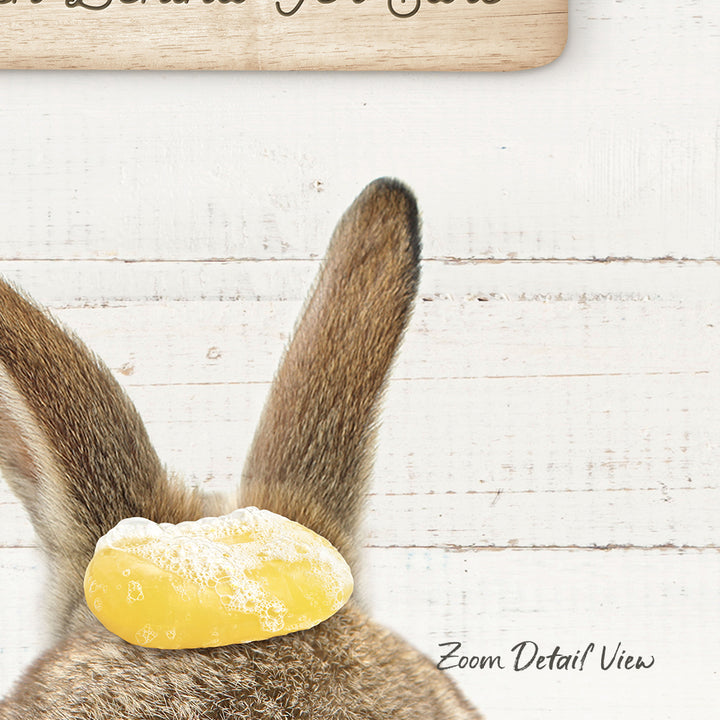 A close-up of a rabbit's head with a yellow object on its ear, against a white wooden background.