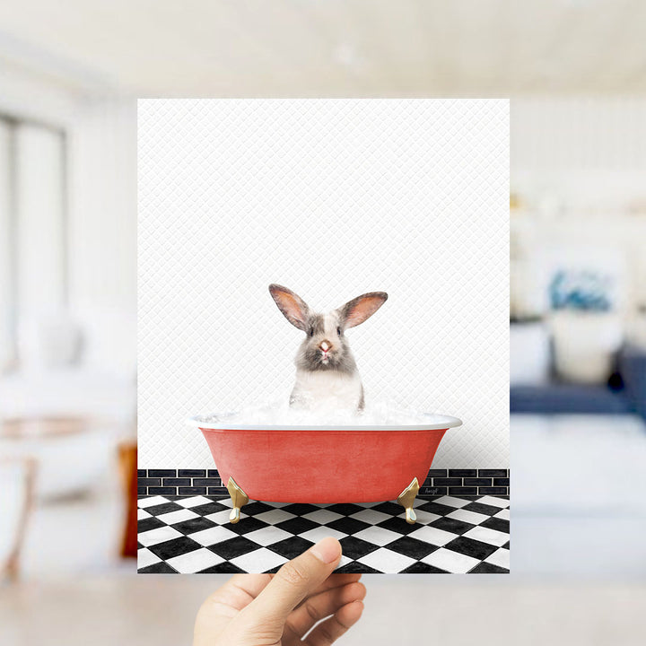 A hand holds up a framed image of a rabbit sitting in a red bathtub filled with water, with a black and white checkered floor in the background.