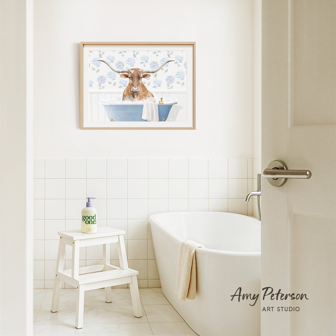 a bathroom with a framed picture of a bull with horns hanging on the wall above a white bathtub.