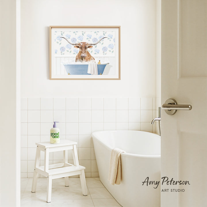 a bathroom with a framed picture of a bull with horns hanging on the wall above a white bathtub.