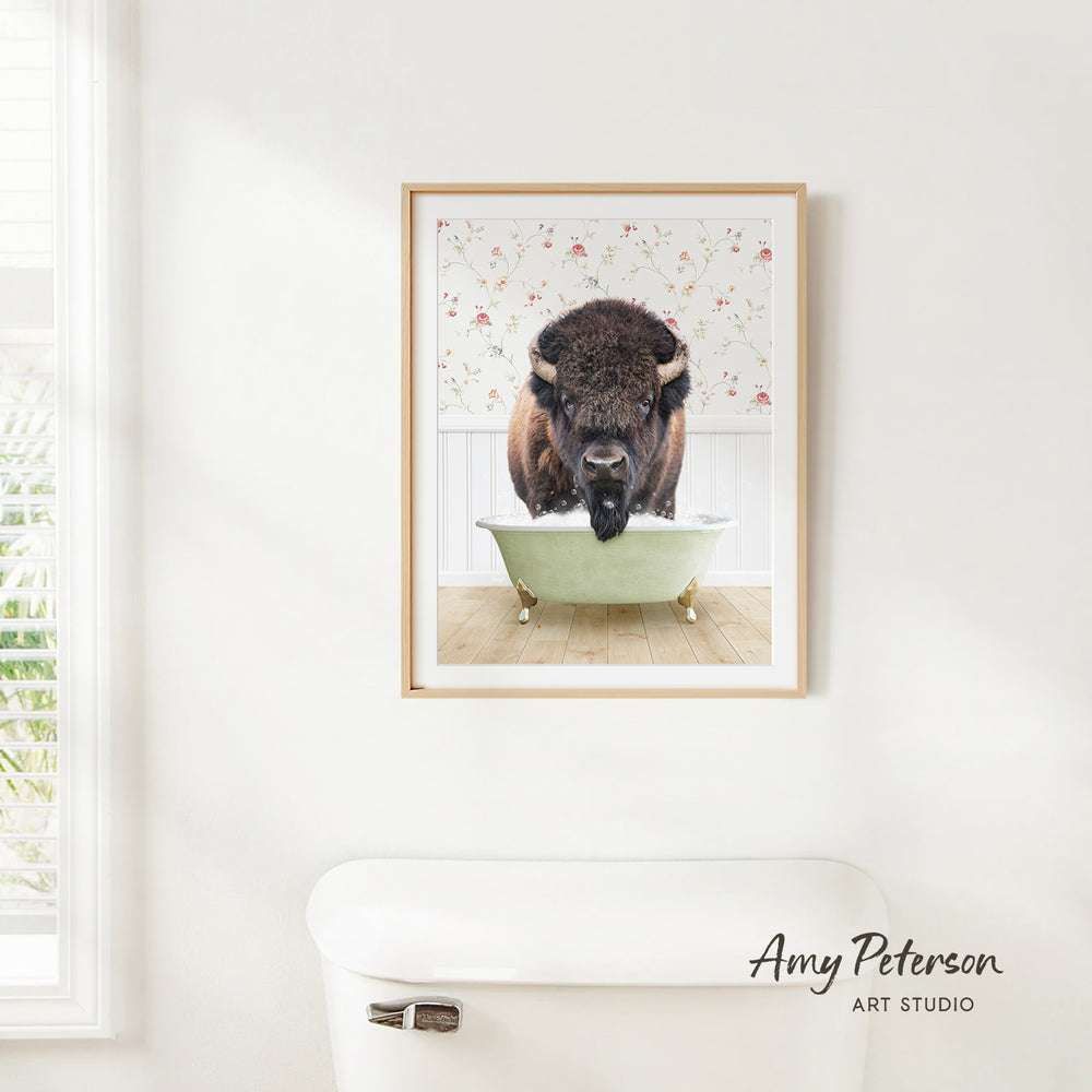 A framed image of a buffalo standing in a bathtub, with a floral pattern on the wall behind it.