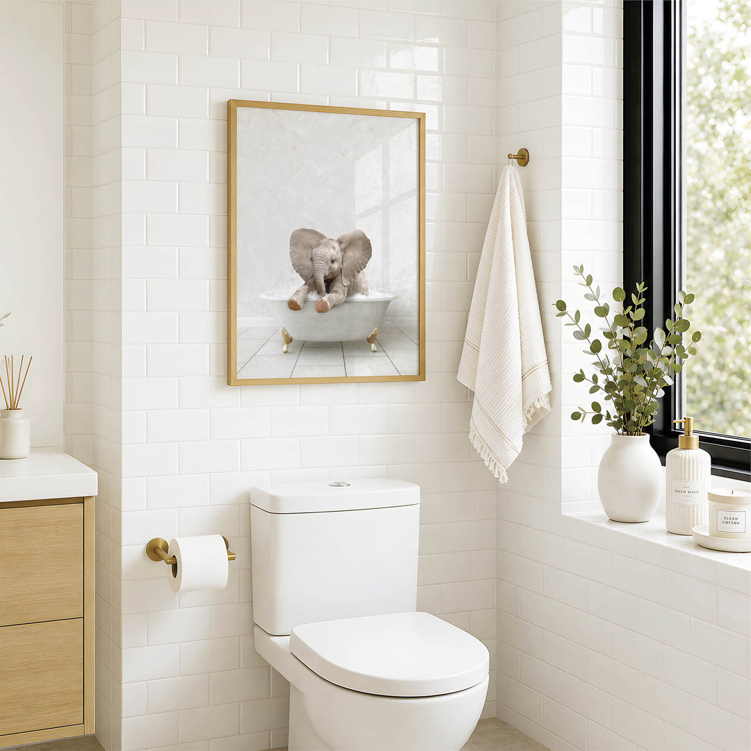 A bathroom with a white toilet, a framed picture of an elephant in a bathtub, and a window with greenery on the sill.
