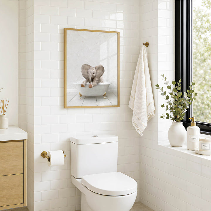 A bathroom with a white toilet, a framed picture of an elephant in a bathtub, and a window with greenery on the sill.