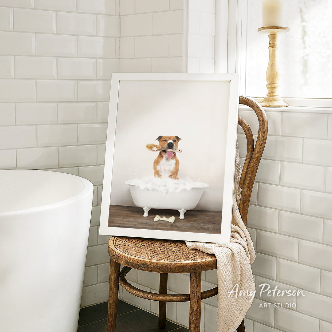 A framed image of a dog sitting in a bathtub, with a towel draped over the back of a chair in a bathroom setting.