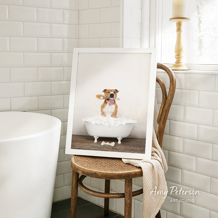 A framed image of a dog sitting in a bathtub, with a towel draped over the back of a chair in a bathroom setting.