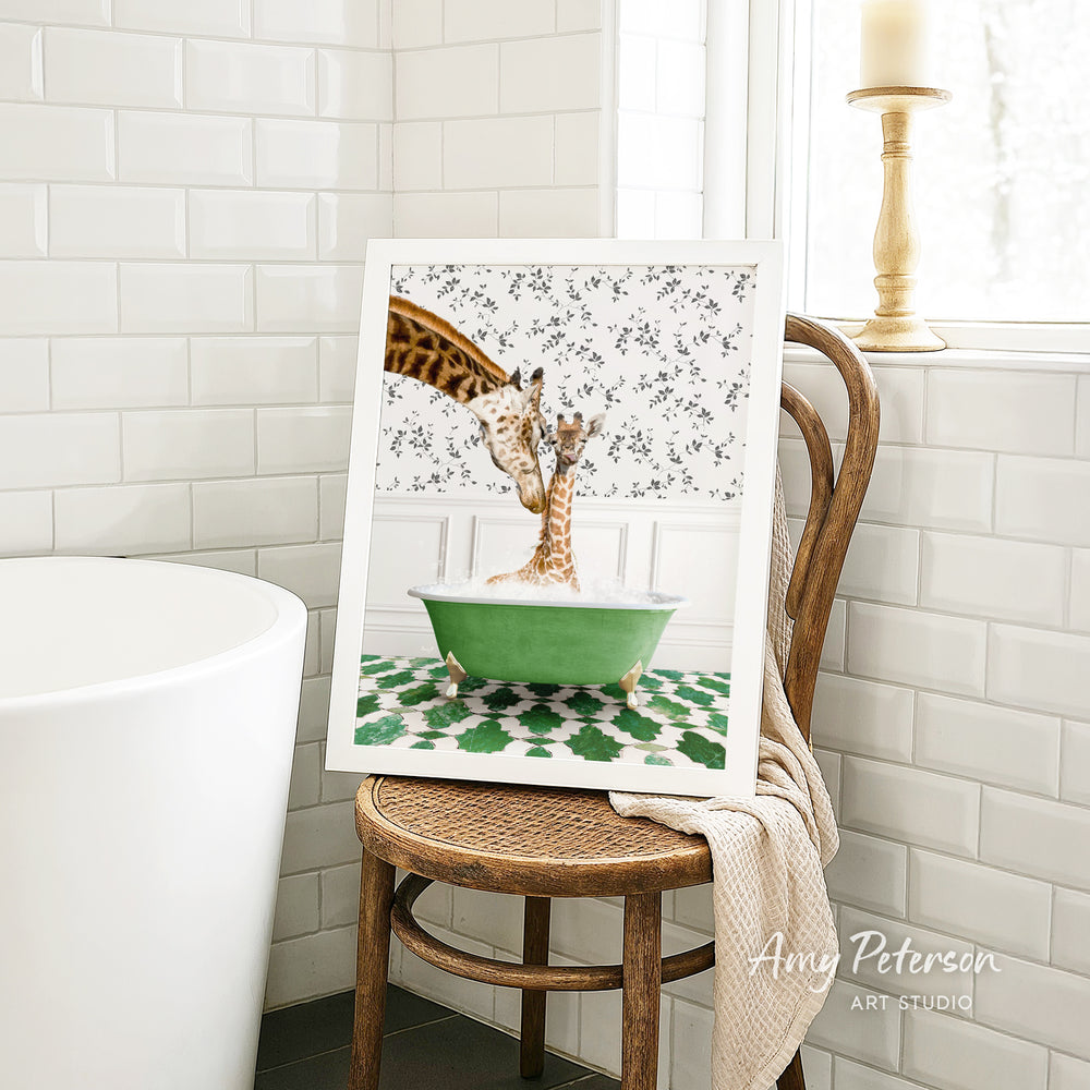 A framed image of two giraffes sitting in a green bathtub, surrounded by a floral pattern, is displayed on a wooden chair in a bathroom setting.